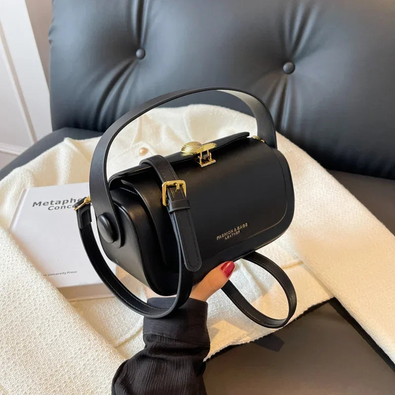 A black leather shoulder bag with gold hardware resting on a white blanket next to a dark leather sofa.