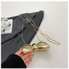 A hand holds a gold-colored acrylic bow clasp mini handbag with a delicate chain strap against a dark gray fabric background.