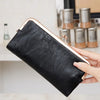 Eine Hand hält eine schwarze Lederclutch mit goldfarbener Schnalle und silberner Hardware.