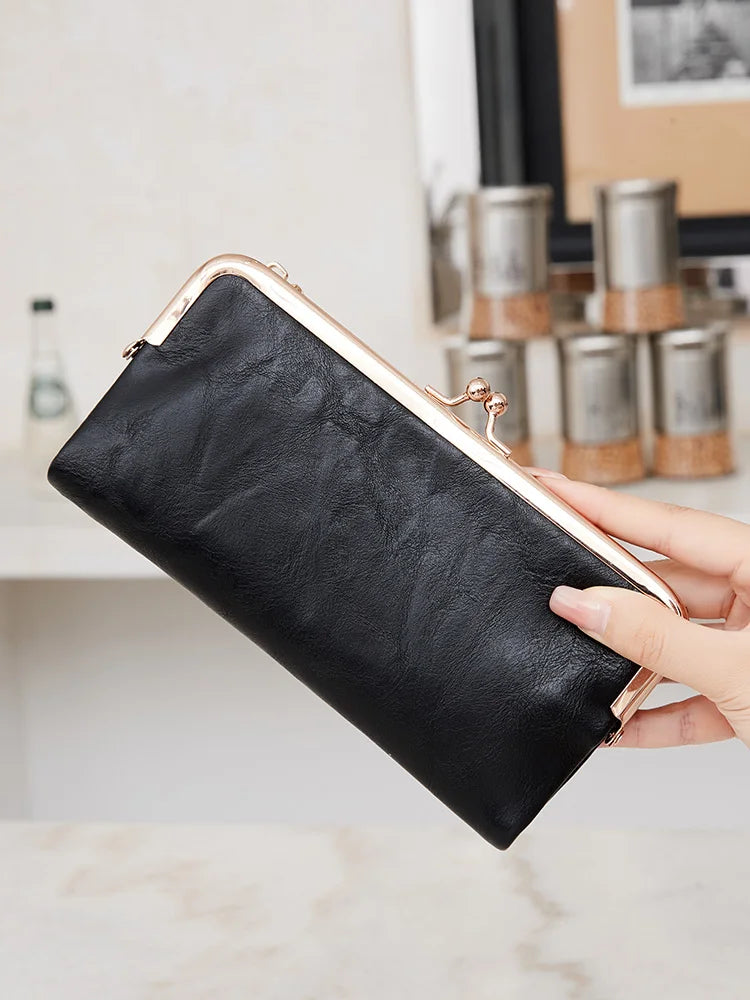 Eine Hand hält eine schwarze Lederclutch mit goldfarbener Schnalle und silberner Hardware.
