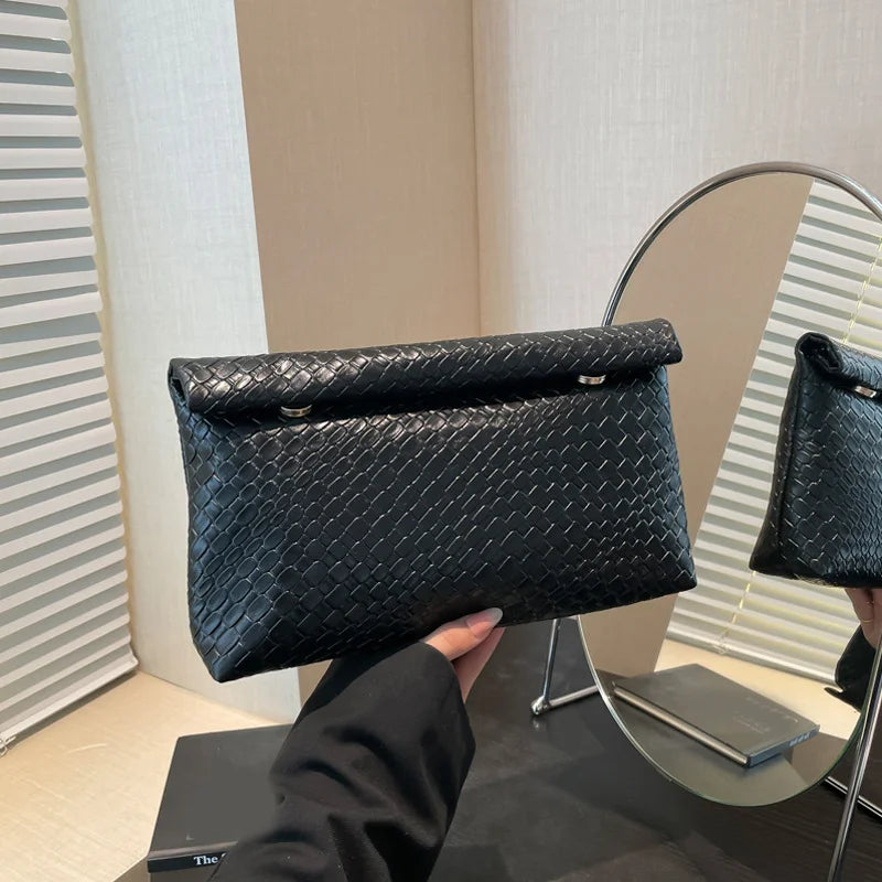 Un bolso de mano tejido negro sostenido contra un espejo con marco de plata.