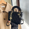 Black quilted leather crossbody handbag with gold chain accents held by a person.