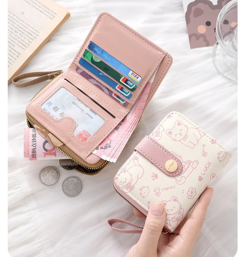 A pink cat cartoon coin purse and card holder wallet with various cards and coins displayed on a white surface.
