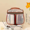 A clear cosmetic bag with a brown leather trim and black and red stripes rests on a stack of books.
