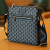 A black men's lightweight crossbody sling bag with a patterned fabric and silver hardware resting on a wooden surface.