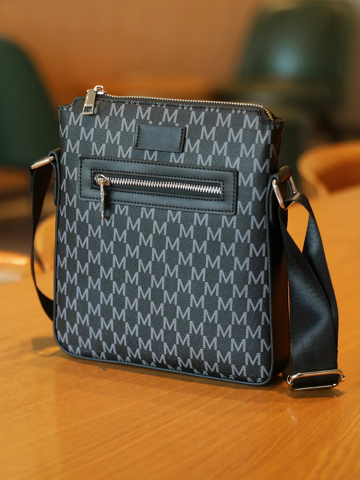A black men's lightweight crossbody sling bag with a patterned fabric and silver hardware resting on a wooden surface.