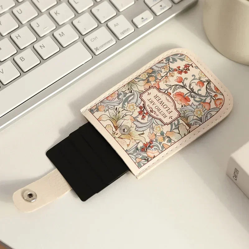 A beige card wallet with a floral pattern rests on a white desk next to a silver laptop keyboard.