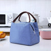 A blue and white striped thermal lunch bag with brown handles resting on a white countertop.