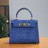 A deep blue crocodile pattern tote bag with a leather handle and gold hardware sitting on a wooden table.