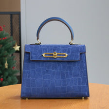 A deep blue crocodile pattern tote bag with a leather handle and gold hardware sitting on a wooden table.