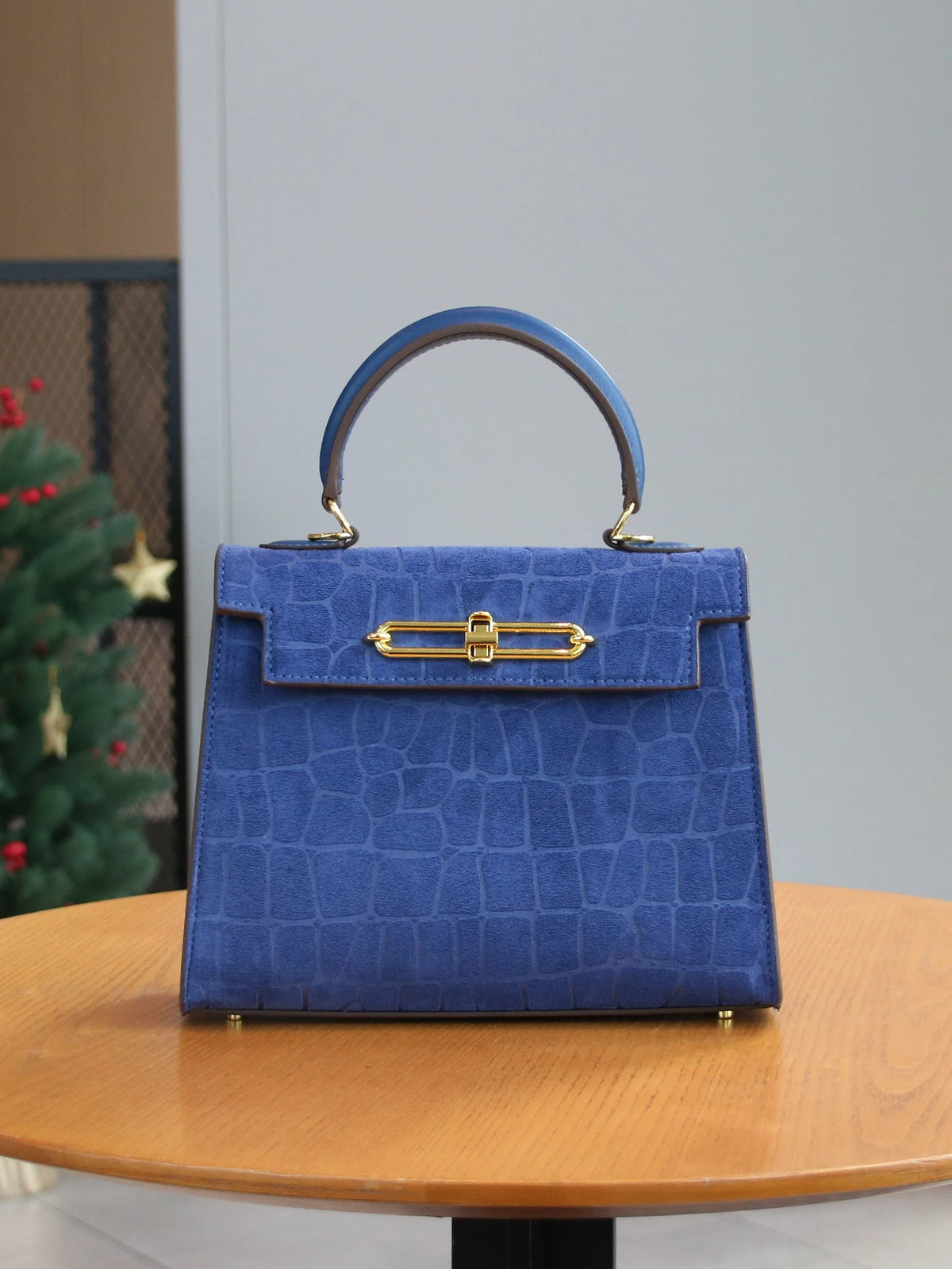 A deep blue crocodile pattern tote bag with a leather handle and gold hardware sitting on a wooden table.