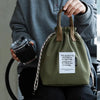 A person holds a olive green waterproof insulated lunch bag with a drawstring and a tag.