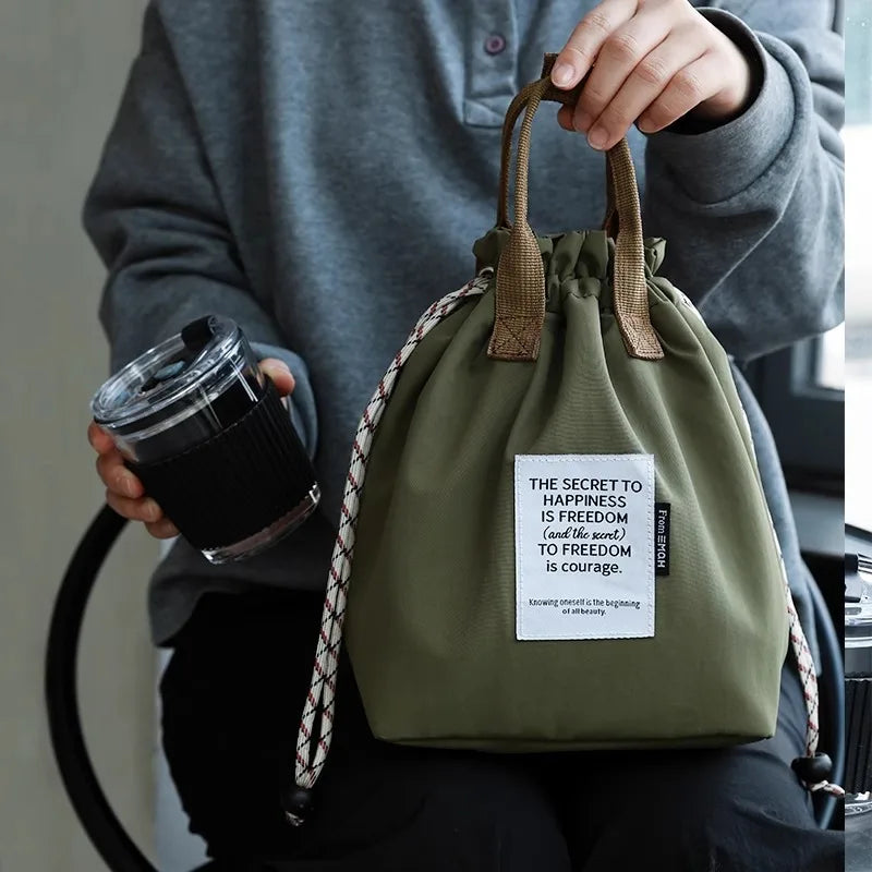 A person holds a olive green waterproof insulated lunch bag with a drawstring and a tag.