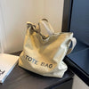 A light beige canvas tote bag with leather straps resting on a dark surface.