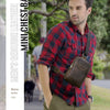A man wearing a red plaid shirt holds a brown leather mini chest bag.