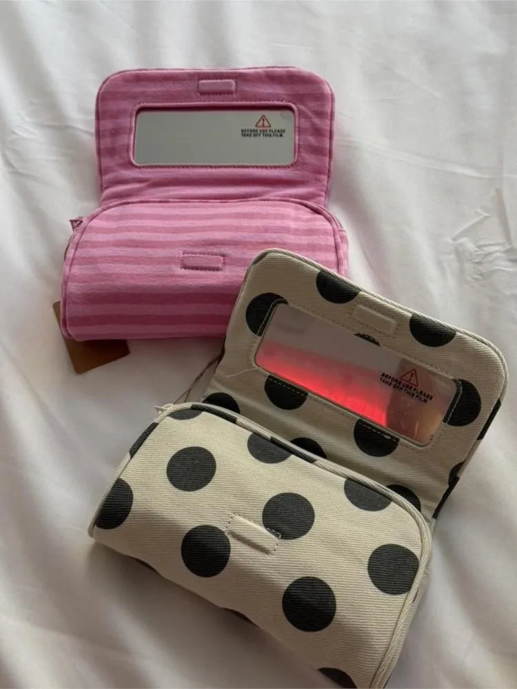 A pink striped makeup bag with a flip-top mirror is shown open on a white surface.