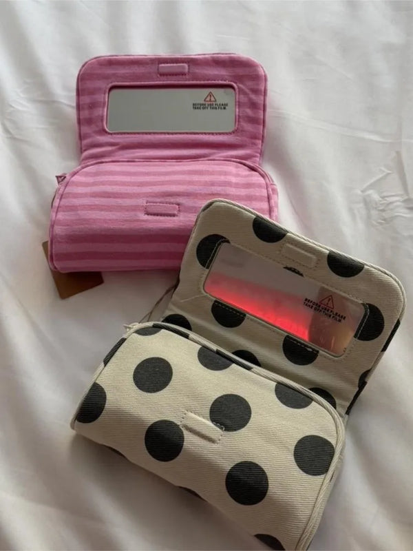 A pink striped makeup bag with a flip-top mirror is shown open on a white surface.