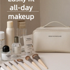 A light beige cosmetic storage bag is shown with various makeup products and brushes on a white surface.