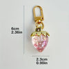 Gold-toned keychain featuring a clear pink strawberry charm and a small cherry bag charm.