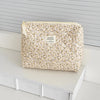 A beige floral print quilted cosmetic bag with a light yellow drawstring and a tag resting on a white surface.