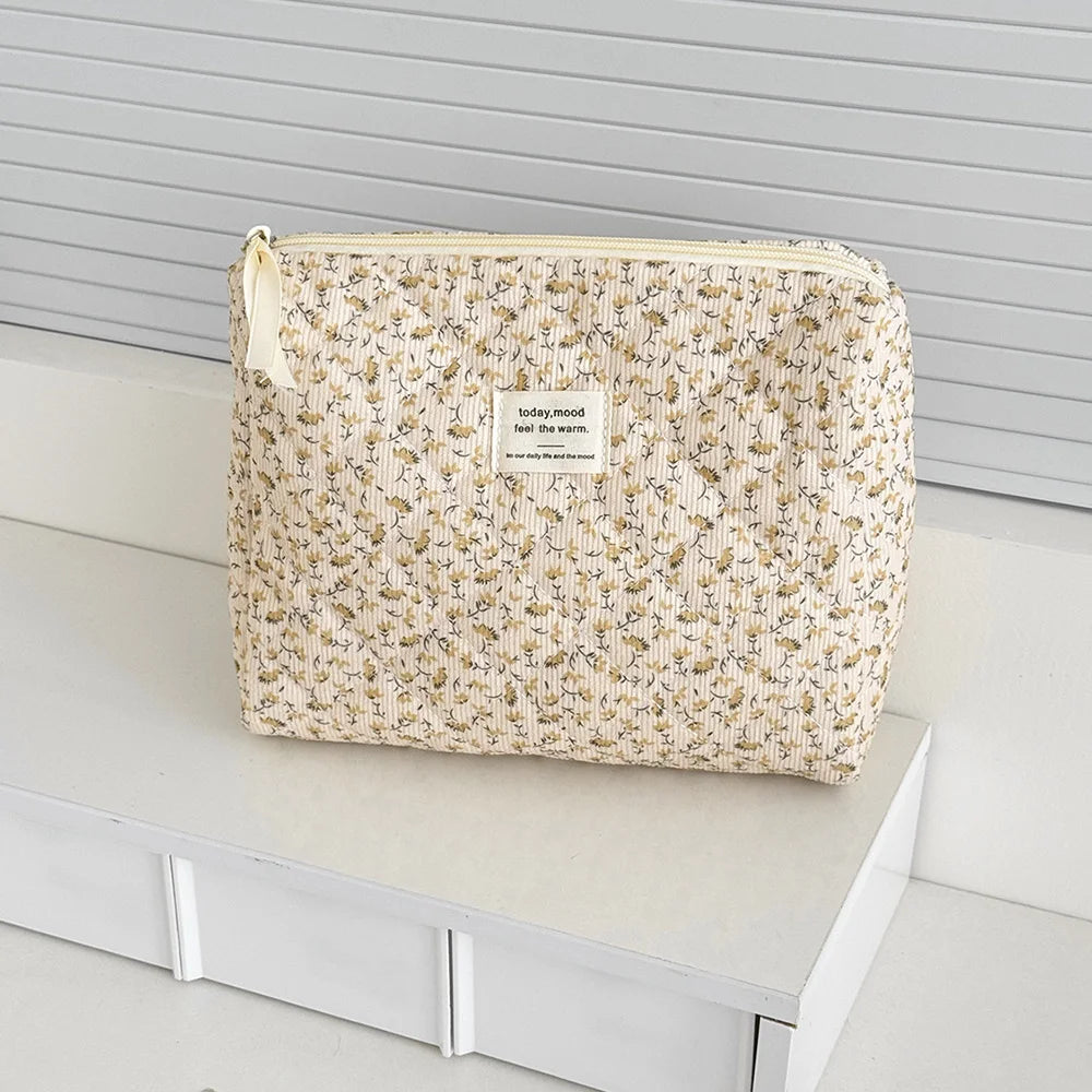 A beige floral print quilted cosmetic bag with a light yellow drawstring and a tag resting on a white surface.