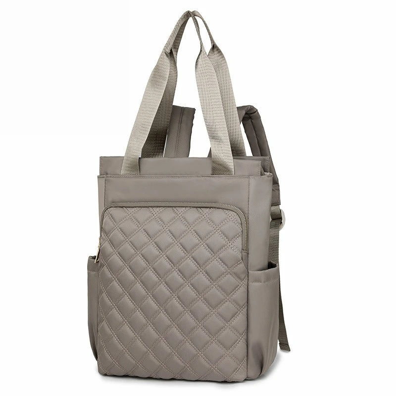 A stylish quilted women's backpack tote in a muted gray color with beige straps.