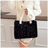 A person holds a black canvas tote bag with a strawberry pattern and light beige handles.
