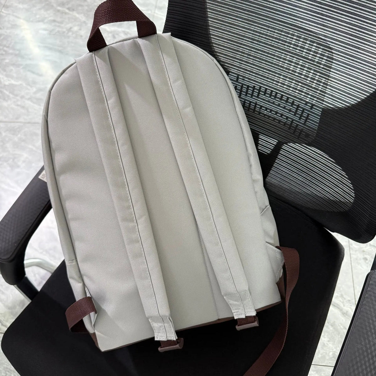 A light beige Pusheen Cat canvas backpack resting on a black chair.