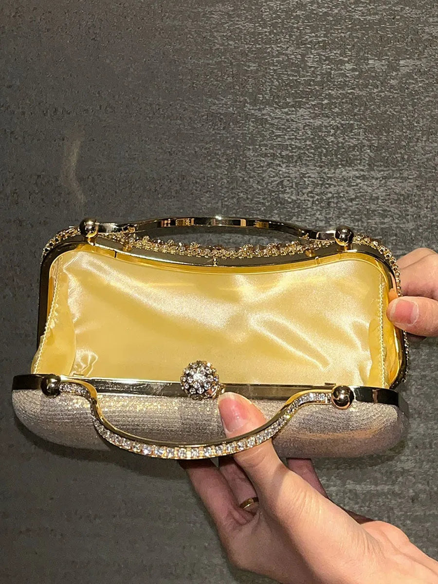 A hand holds an elegant gold and silver clutch bag decorated with diamond rhinestones and a golden tassel.