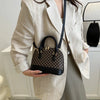 A woman wearing a beige blazer holds a black checkered leather shoulder bag with a black strap.