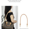 A brown leather handbag with a matching strap is shown being carried by a woman against a white background.