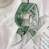 Foulard pour cheveux floral en soie vert et blanc, noué en nœud, exposé sur une chemise blanche et à côté d'un livre.