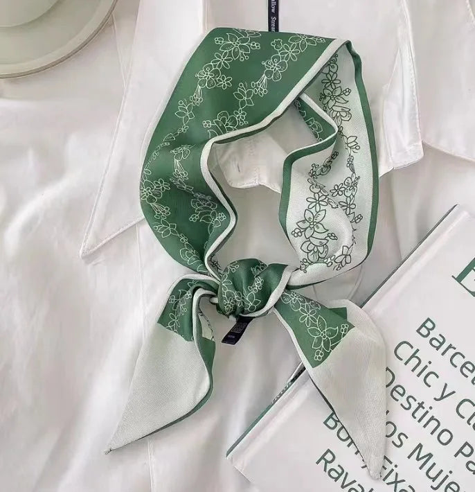 Foulard pour cheveux floral en soie vert et blanc, noué en nœud, exposé sur une chemise blanche et à côté d'un livre.