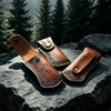 A brown leather knife sheath with a belt loop is resting on a dark gray rock.
