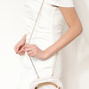 A woman wearing a white dress holds an elegant gold-tone evening clutch bag with a light, translucent finish.