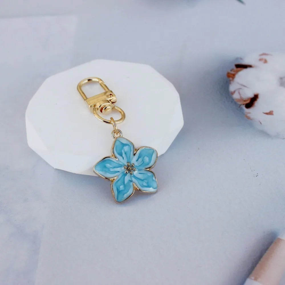 A gold-colored resin flower keychain with blue and white coloring rests on a white ceramic tile.