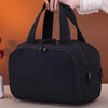 A hand is holding a black portable side-zip cosmetic organizer bag against an orange background.