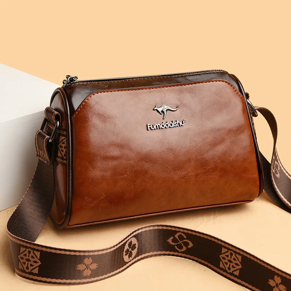 A brown leather shoulder bag with a dark brown strap and a silver embossed logo on a light background.