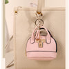 Pink portable earbud case attached to a beige leather handbag with a gold keychain charm