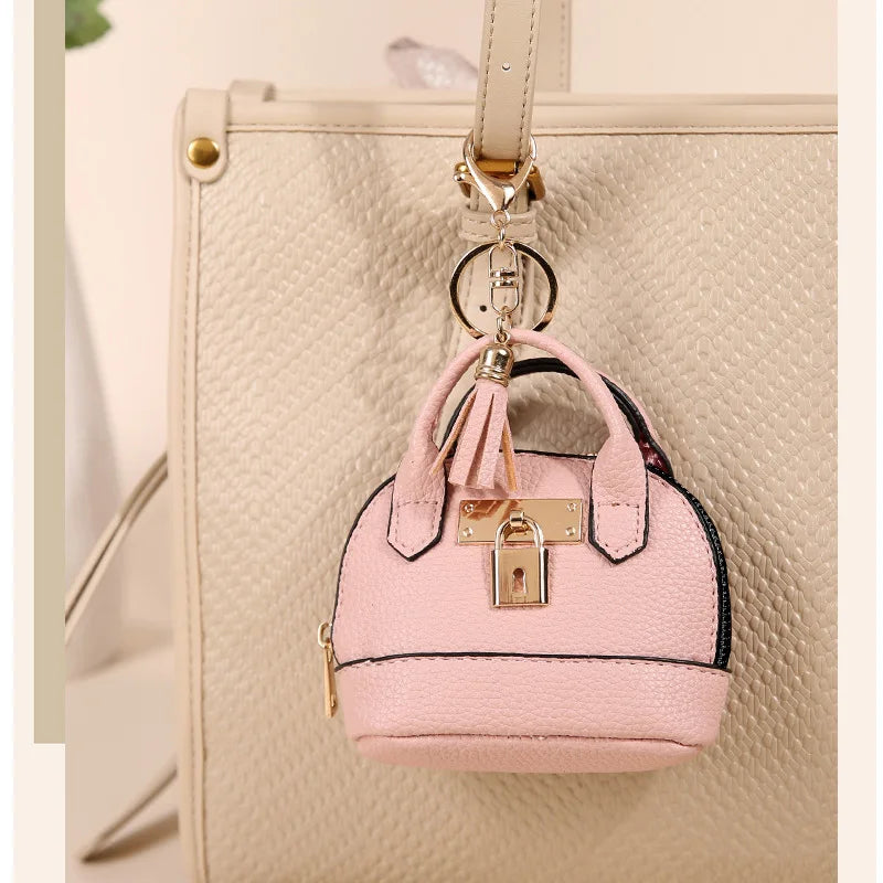 Pink portable earbud case attached to a beige leather handbag with a gold keychain charm