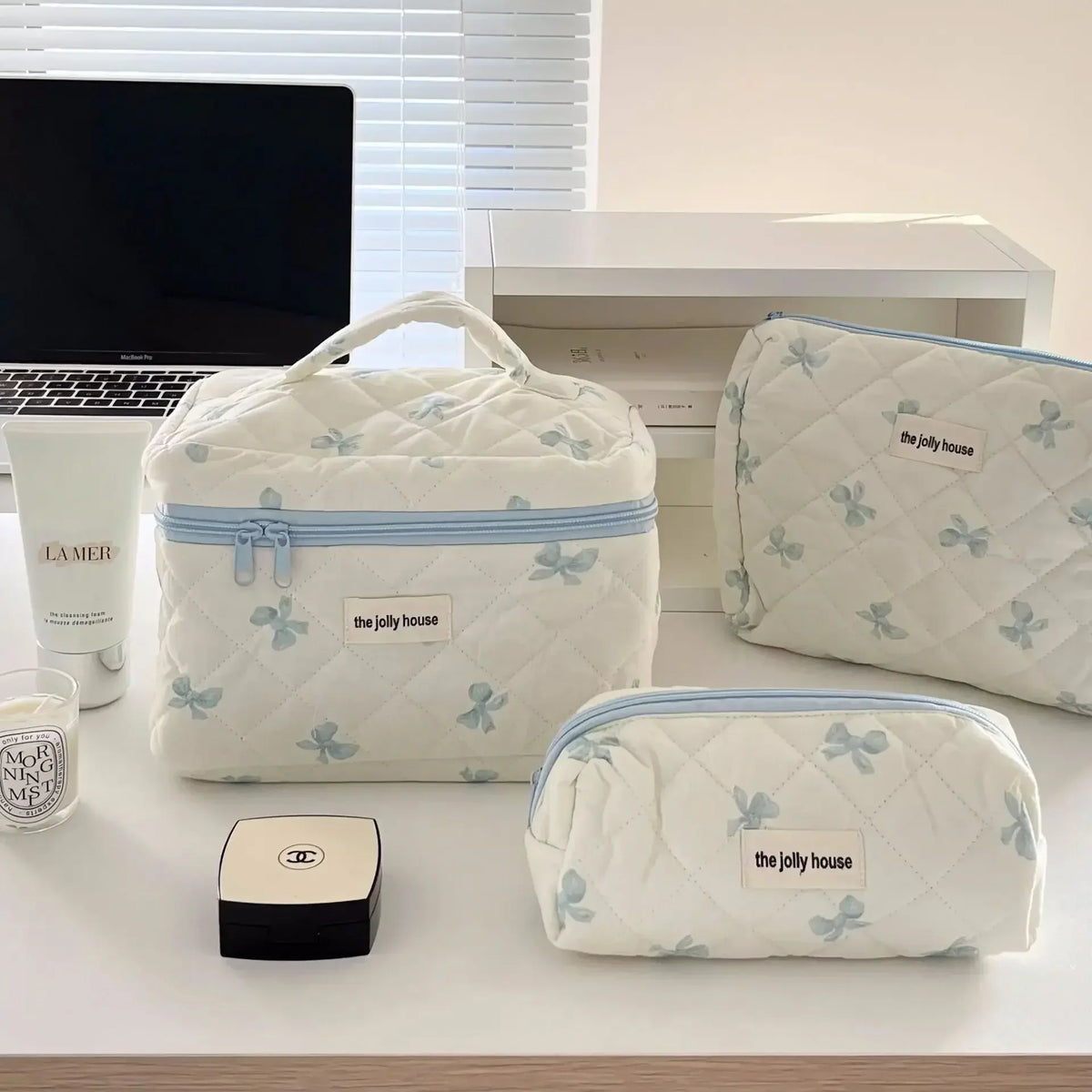 Sac de rangement cosmétique matelassé blanc avec motif nœud bleu et logo Jolly House posé sur une table blanche.