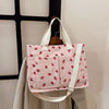 Pink canvas tote bag featuring a pattern of red strawberries on a white background.