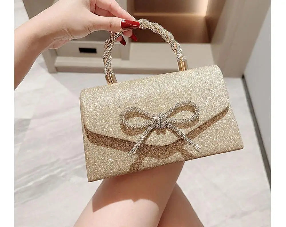 Una mano sostiene un bolso de fiesta con lazo brillante dorado y textura.