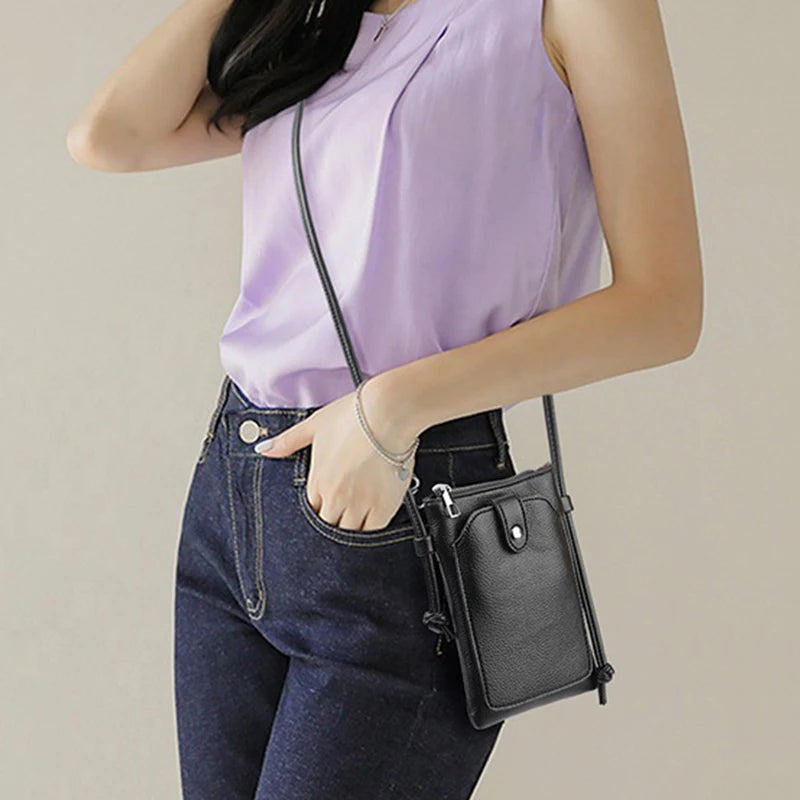 A woman wearing a light purple top and dark jeans holding a black compact PU leather crossbody bag.