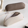 A beige makeup pouch and a gray cosmetic pencil case are displayed on a white surface.