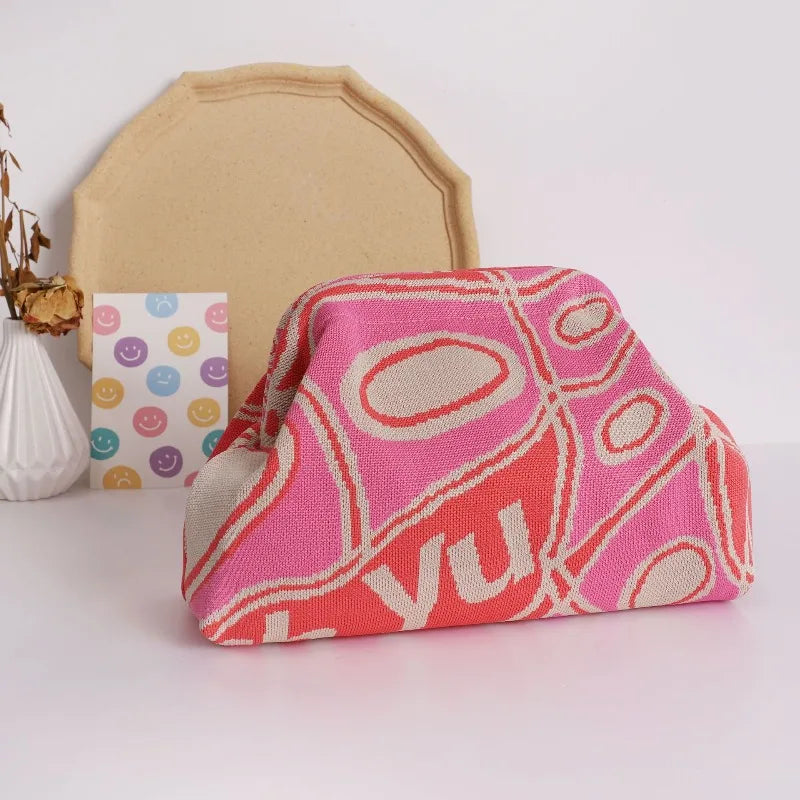 A pink and orange knitted clip bag resting on a white surface next to a beige fabric piece.