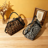 A brown leopard print faux leather handbag with a top handle and crossbody strap resting on a wooden surface.