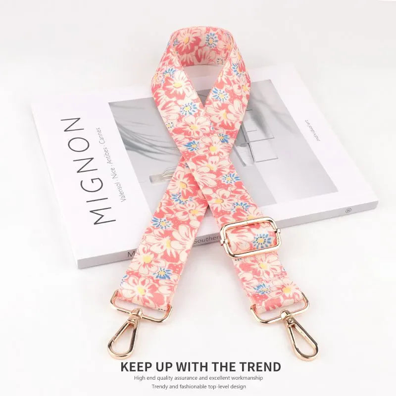 Pink floral patterned diagonal scarf or strap with a gold buckle displayed on a white box.