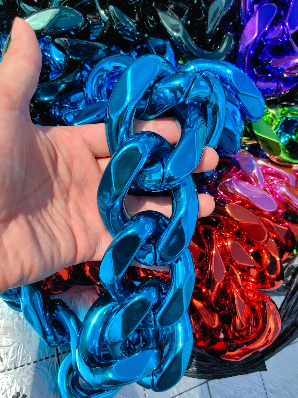 A hand holds a chunky blue acrylic Cuban link necklace for men, showcasing the shiny metal links.