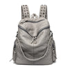 Sac à dos en cuir souple gris clair et rivetée avec plusieurs sangles et clous décoratifs.